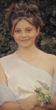 An 8-year-old girl wears a formal white dress and a corsage on her wrist. 